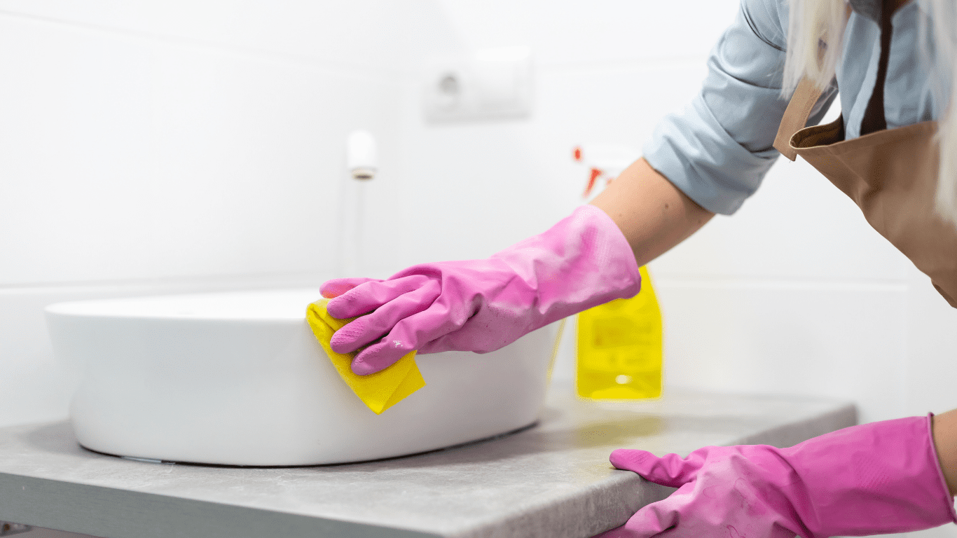Person cleaning a white sink with a yellow cloth while wearing pink rubber gloves, emphasizing professional cleaning services for residential and commercial spaces in Melbourne.