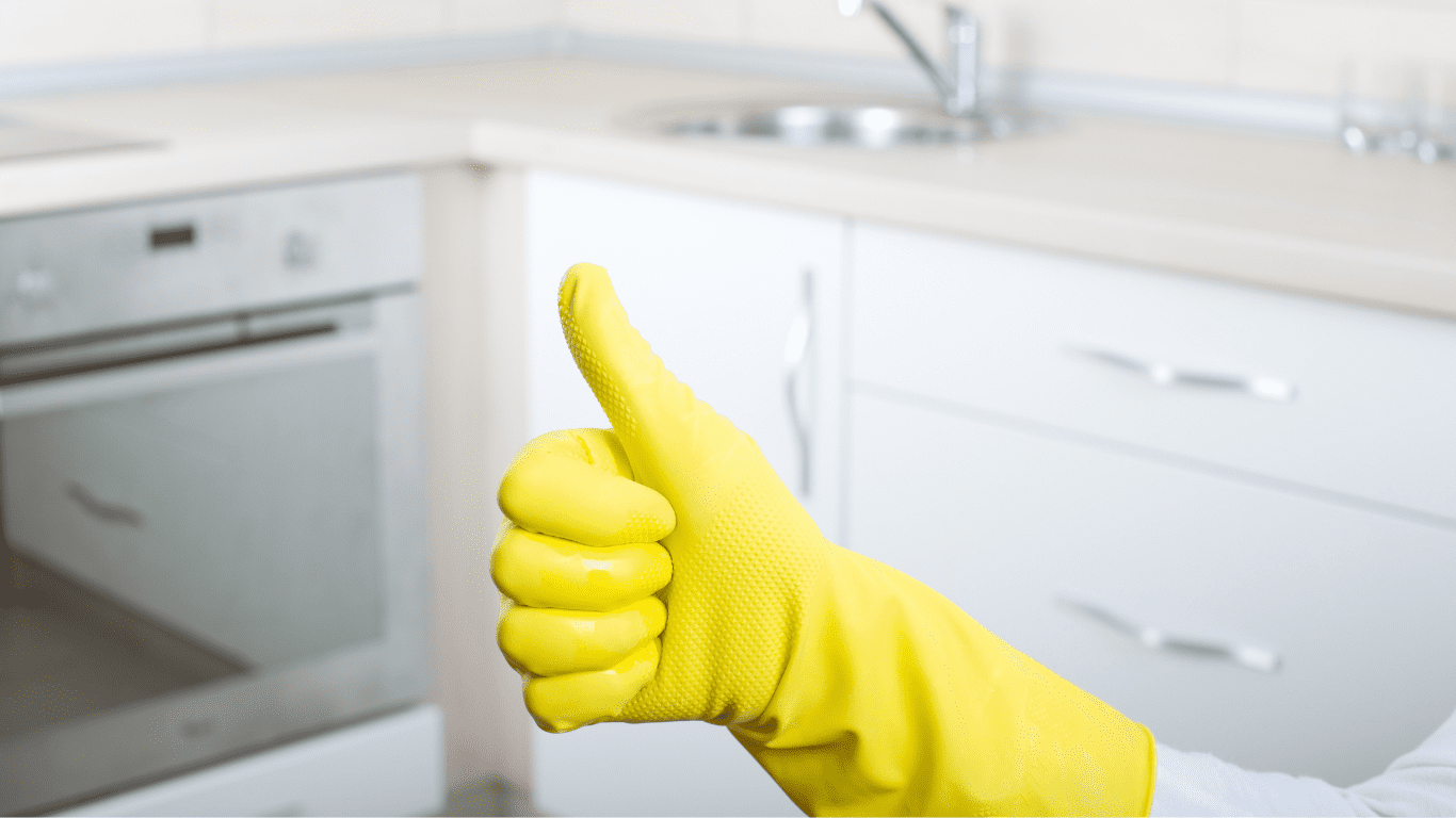 Thumbs up gesture in yellow cleaning glove, symbolizing satisfaction and quality in professional cleaning services, with a clean kitchen background reflecting Deep Clean King's commitment to hygiene and safety standards.