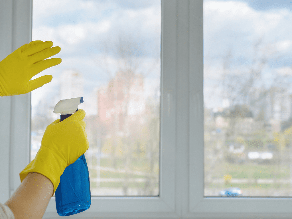 Person wearing yellow gloves holding a spray bottle, preparing to clean a window in a residential building, emphasizing professional cleaning services for strata properties in Melbourne.