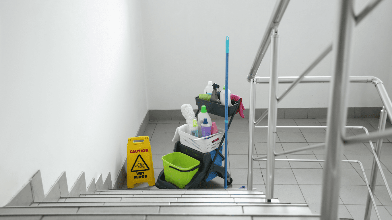 Cleaning supplies and equipment on a stairwell, including caution sign for wet floor, emphasizing professional strata cleaning services in Melbourne.